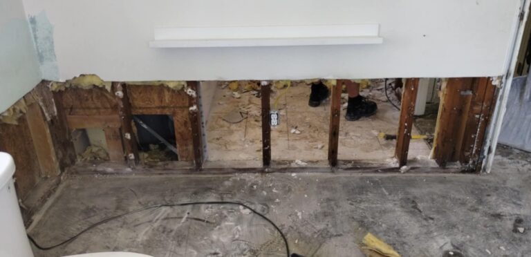 The bottom portion of a drywall wall has been cut away to expose the interior framing studs during water damage restoration.
