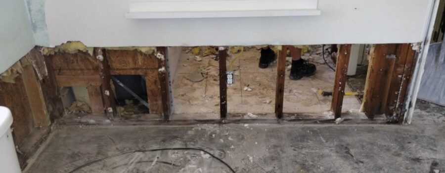 The bottom portion of a drywall wall has been cut away to expose the interior framing studs during water damage restoration.