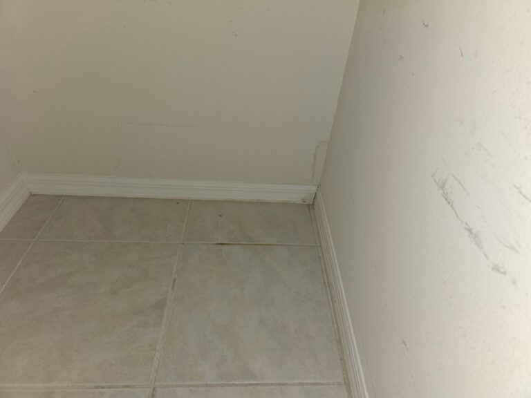 A water stain is visible along the corner of a beige wall near the baseboards and tile flooring.