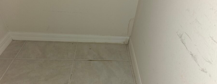 A water stain is visible along the corner of a beige wall near the baseboards and tile flooring.