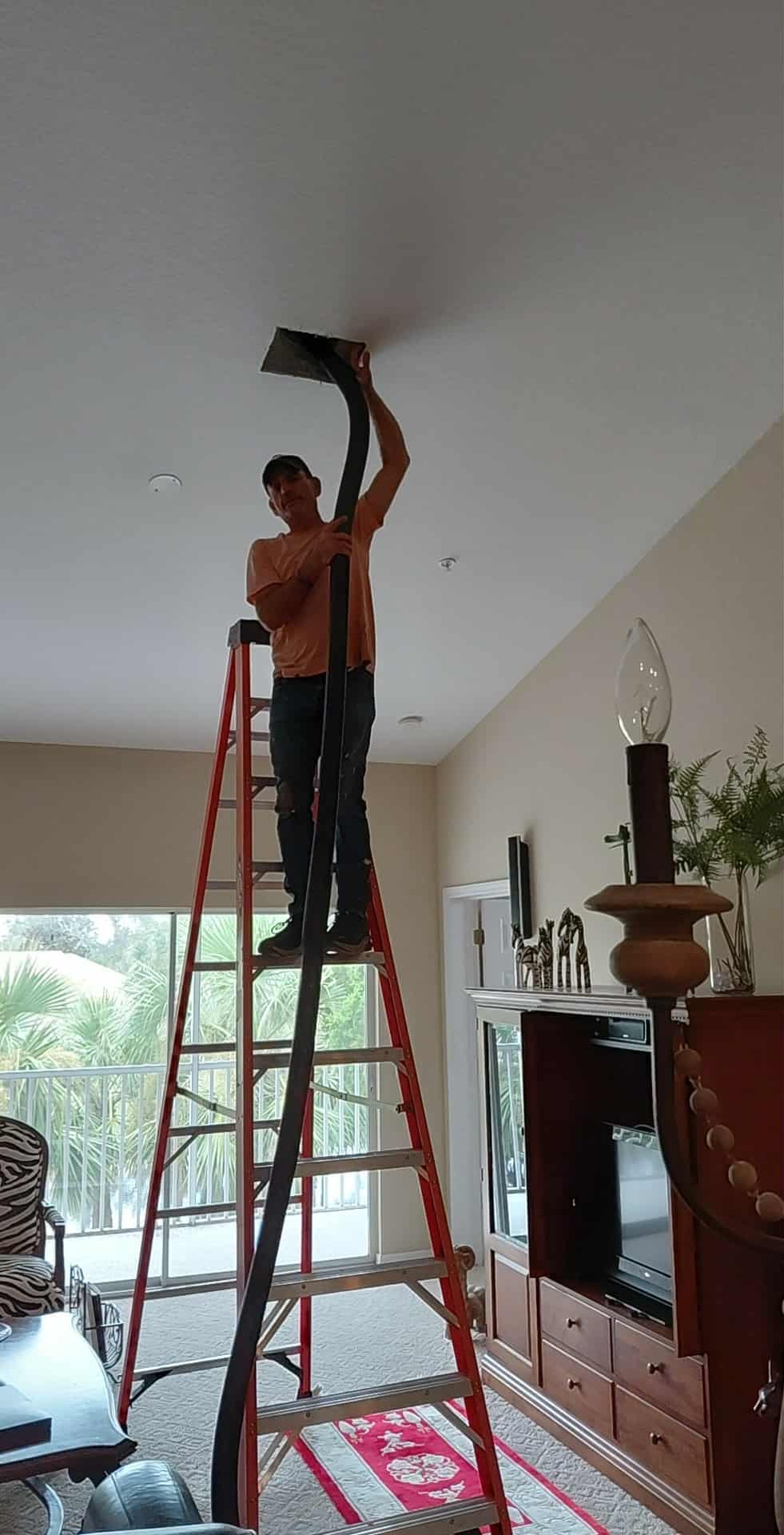 Technician using specialized duct-cleaning equipment through a ceiling HVAC access opening in a Sarasota home.